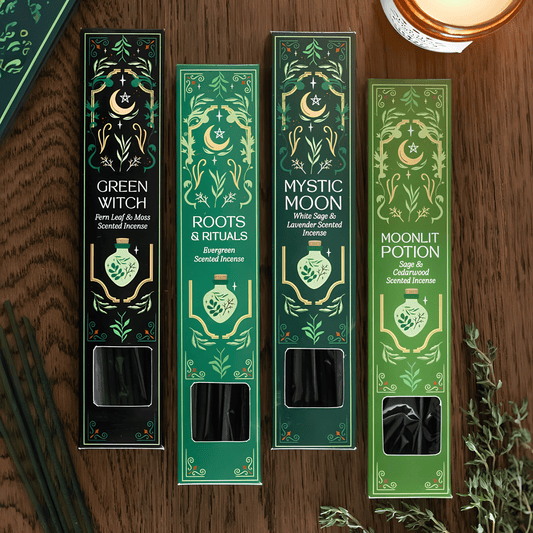 Four tall rectangular scented incense boxes arranged on a wooden surface, each with ornate green and gold illustrated packaging and visible incense sticks through a window near the bottom. The box labels read Green Witch, Roots & Rituals, Mystic Moon, and Moonlit Potion.