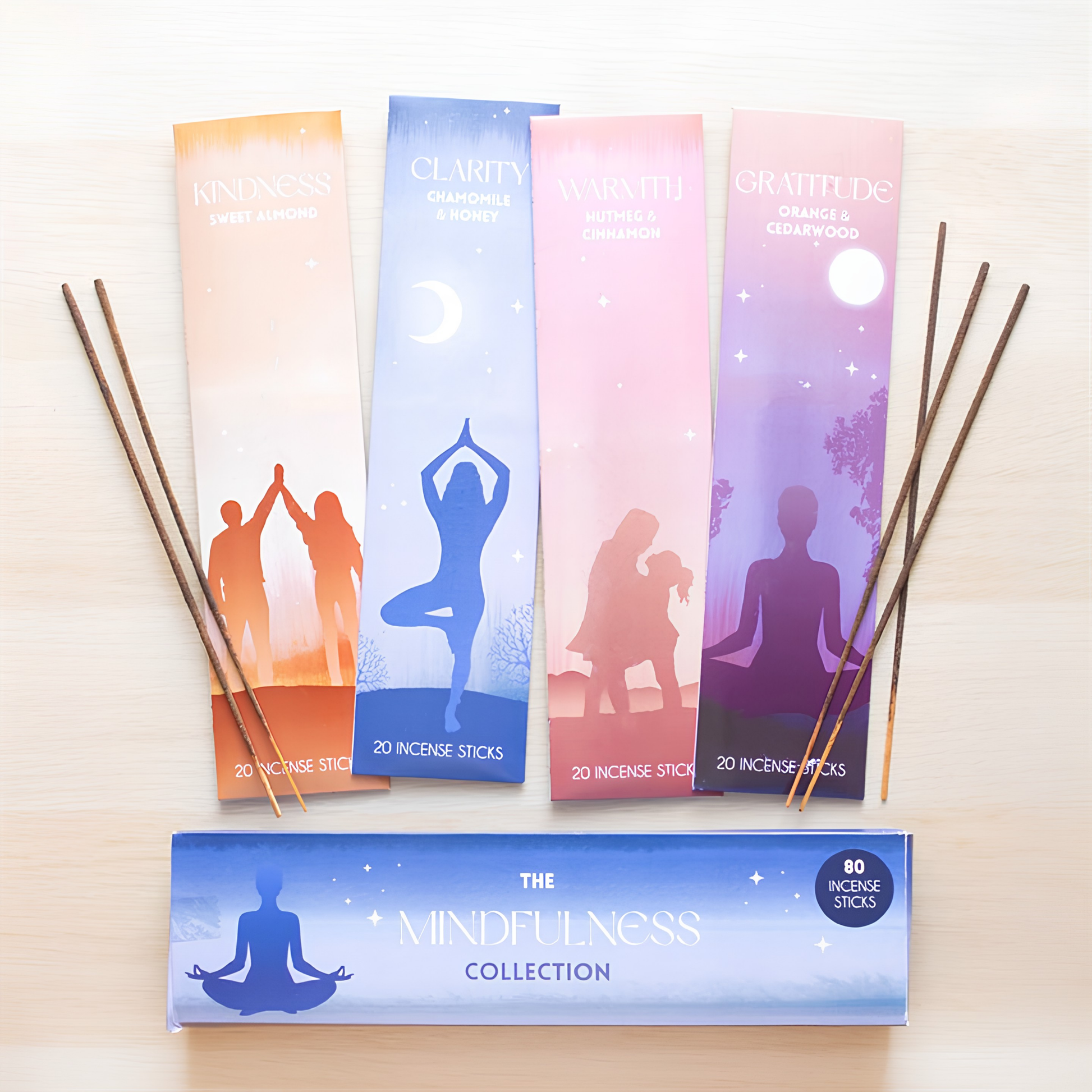 Four vertical incense packet cards in orange, blue, pink, and purple are arranged on a light wood surface with incense sticks leaning against them. A blue box labeled 'The Mindfulness Collection' sits at the bottom.