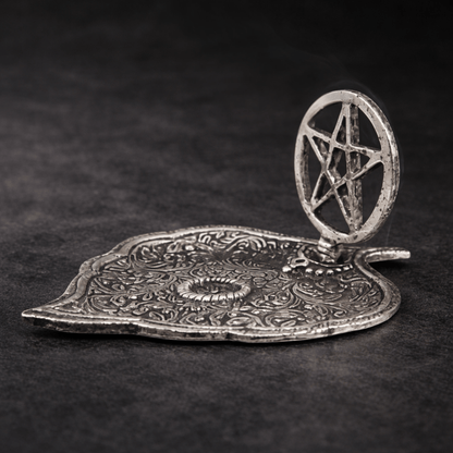 Silver incense holder tray shaped as a leaf and a pentagram in a circle on the one end on a black background 