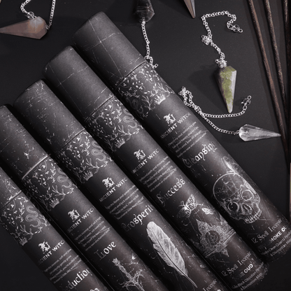 Black cylindrical containers with decorative labels on a dark surface with crystals and jewelry.