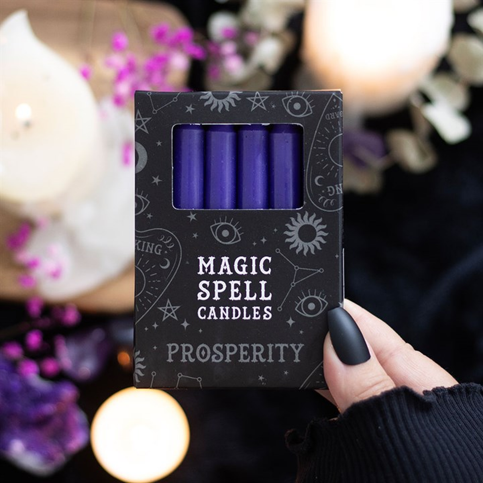 Box of 'Magic Spell Candles Prosperity' held by a hand with a blurred candlelit background.