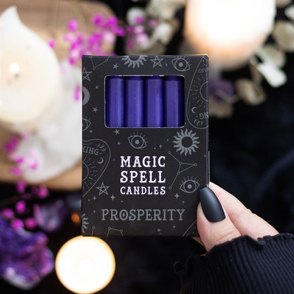 Box of 'Magic Spell Candles Prosperity' held by a hand with a blurred candlelit background.