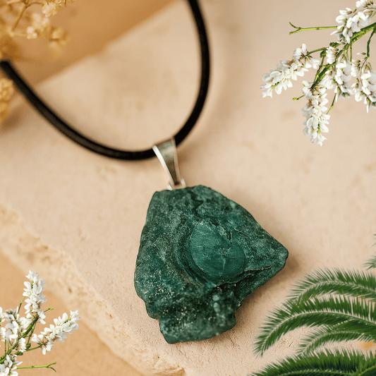 Green stone pendant on a black cord with white flowers and green leaves in the background