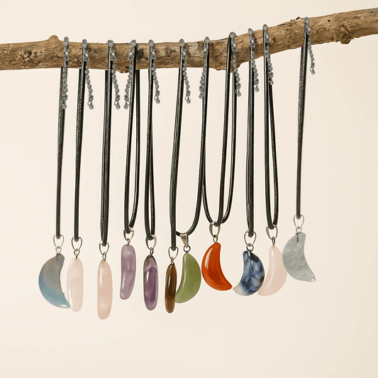 Assorted crescent moon gemstone pendants on a black faux leather cord necklace with an extender chain on the lobster clasp and they are hanging next to each other from a branch