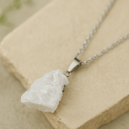 white moonstone rough pendant on a link chain on a beige stone and beige background.