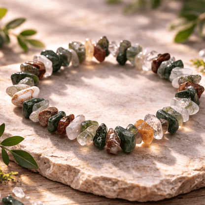 Multicolored stone bracelet of greens and earthy browns on a stone surface with green leaves