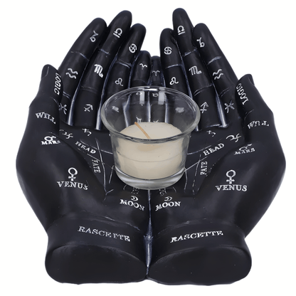 Black resin hands with astrological symbols holding a small glass container with a candle on a white background
