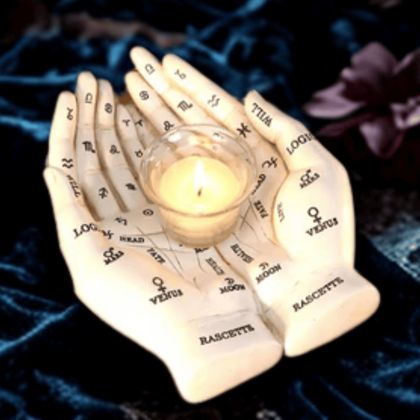 Hand holding a small glass container with a candle inside, on a dark fabric background