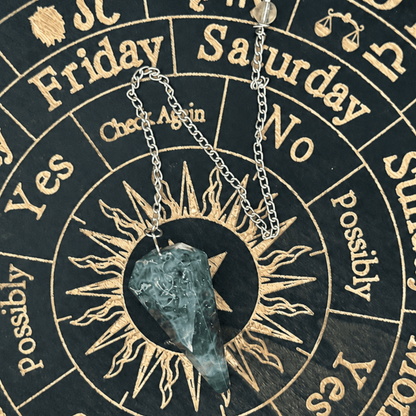 A silver chain necklace with a tumbled, pointed teal-green crystal pendant, displayed on a black and gold zodiac wheel background.