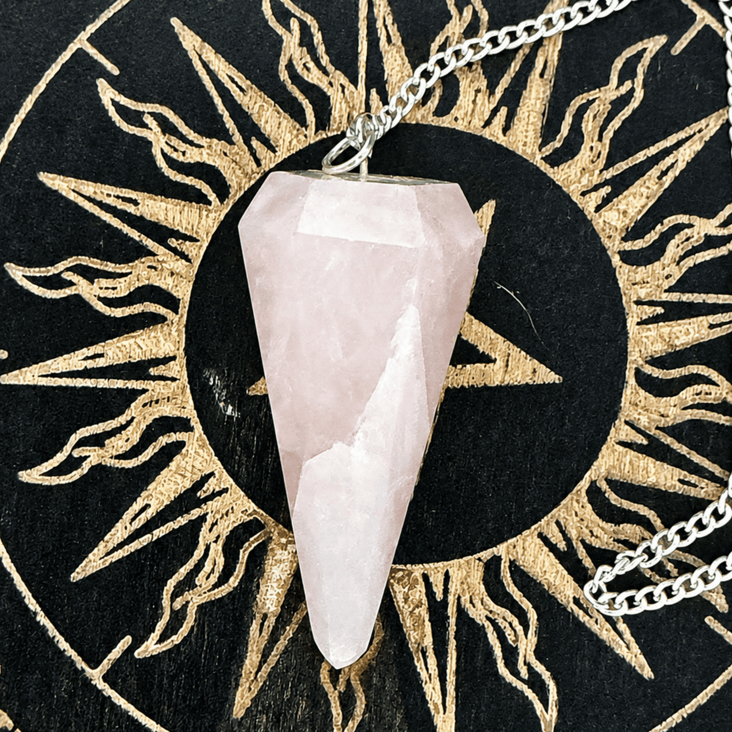 A silver chain pendulum with a pink rose quartz crystal facet point