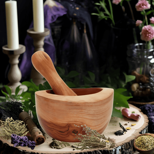 Teak Pestal & mortar sitting on a wooden board surrounded by herbs, leaves and unlit candles in candle sticks.