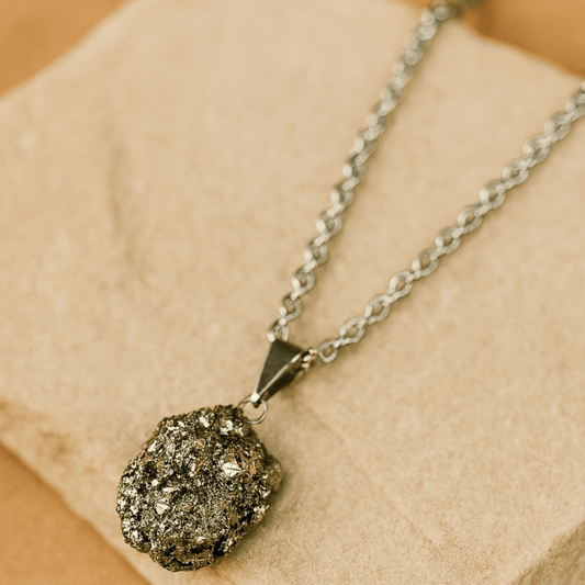 Necklace with a rough pyrite (fools gold) pendant on a stainless steel chain on a beige background