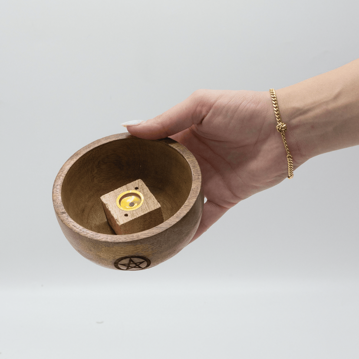 Video of a hand holding a wooden bowl and turning it to its side so you can see the inside where there is a small wooden  box shape with a gold looking circle on the wooden box.