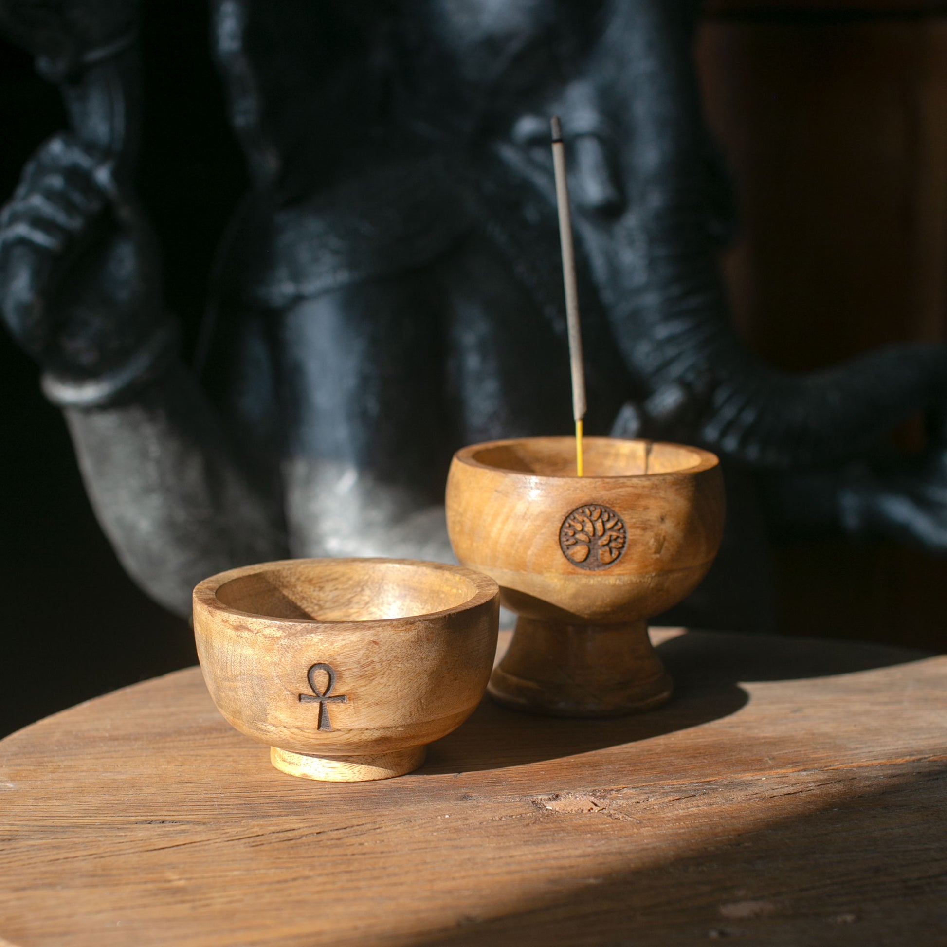 Two wooden incense holders with a candle and an ankh symbol on a wooden surface.