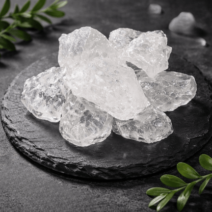 Clear crystal rocks on a dark slate surface with green leaves.