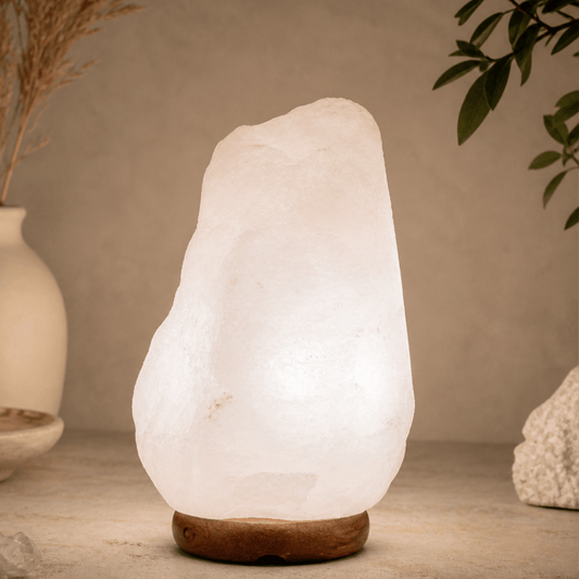 White salt lamp with a textured surface on a wooden surface, surrounded by plants and a vase.