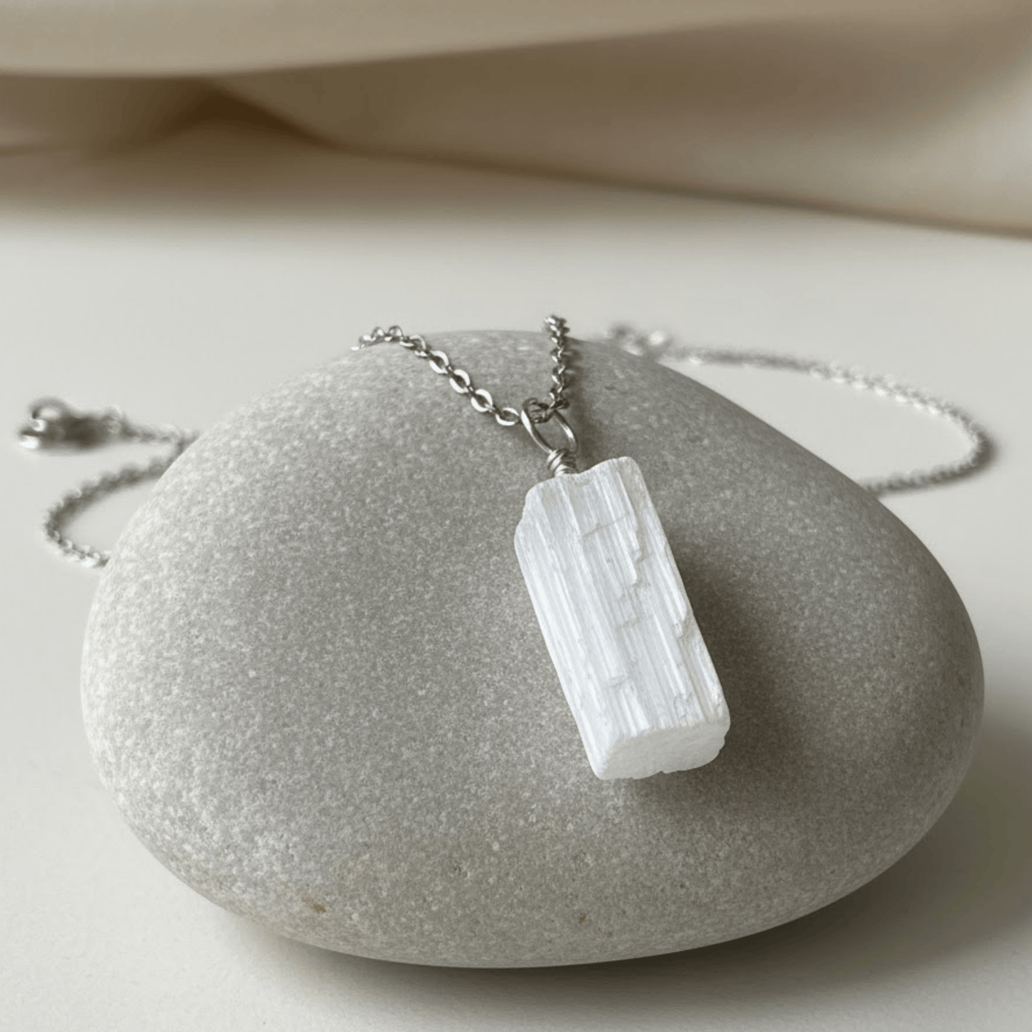 Necklace with a rectangular rough white selenite crystal pendant on a stone surface