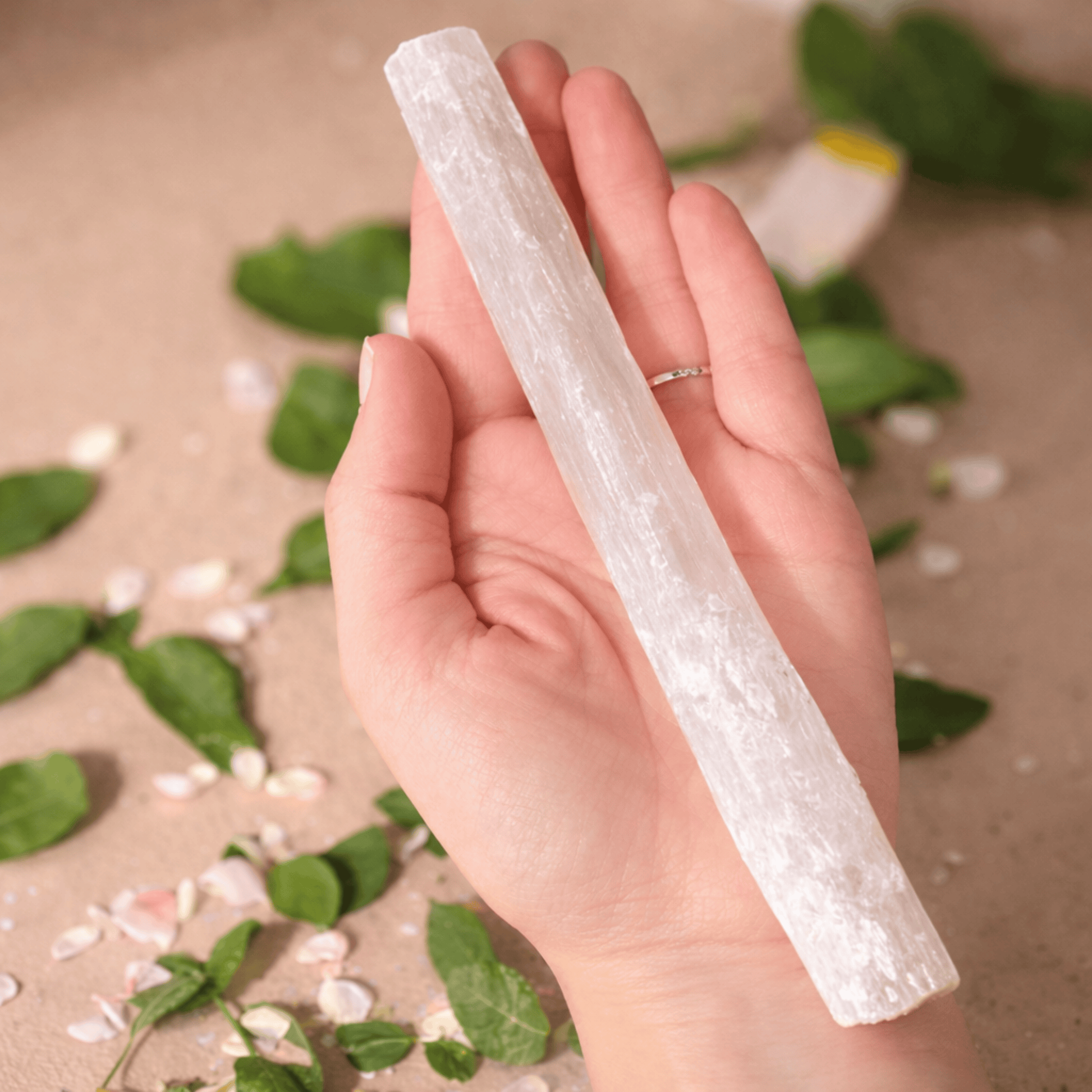 Hand holding a cylindrical crystal-like object with a natural background of green leaves and white flowers.
