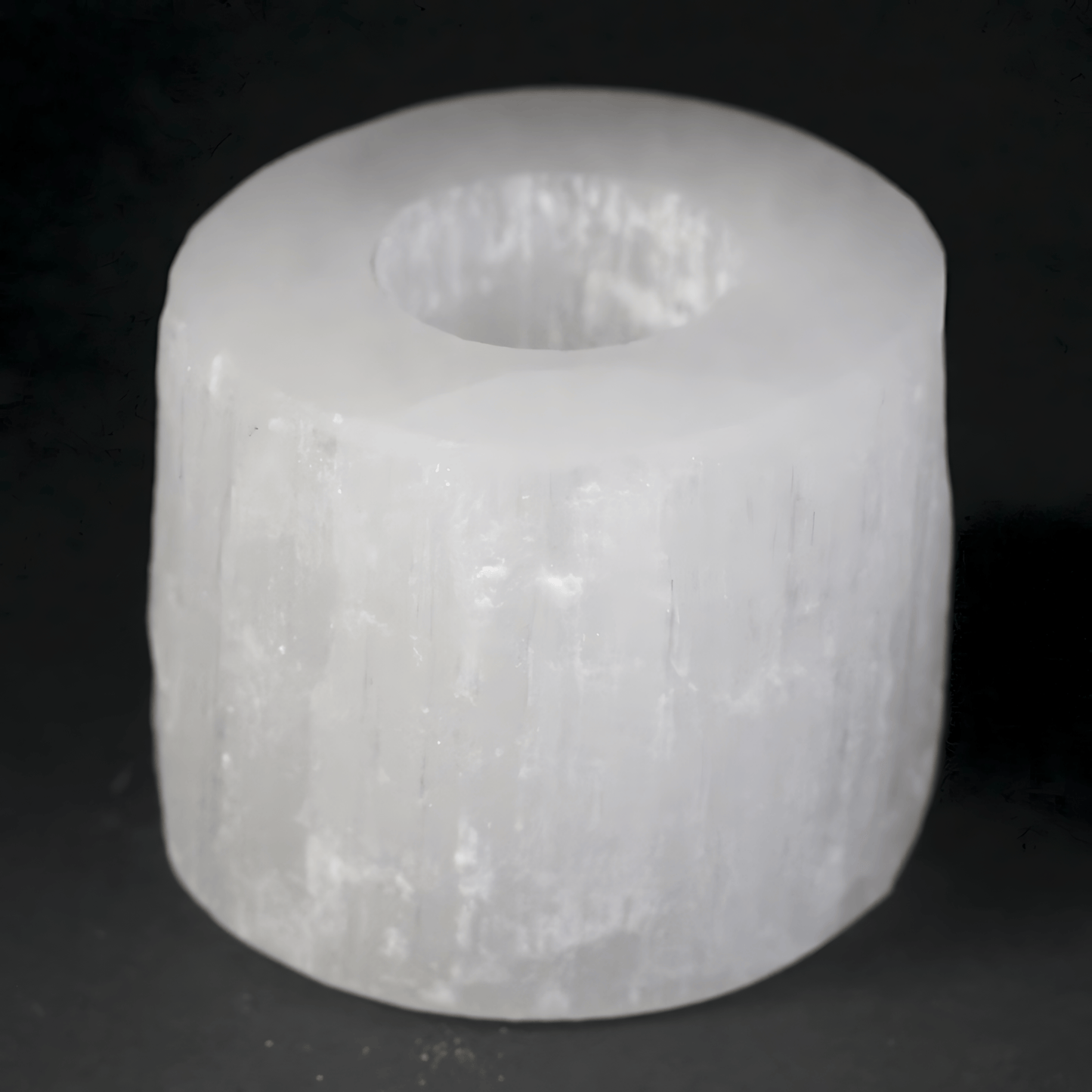 White Selenite cylindrical object with a central hole on a black background