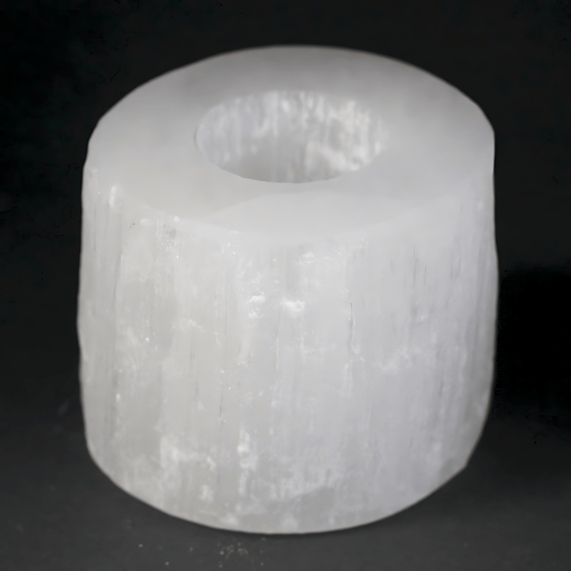 White Selenite cylindrical object with a central hole on a black background