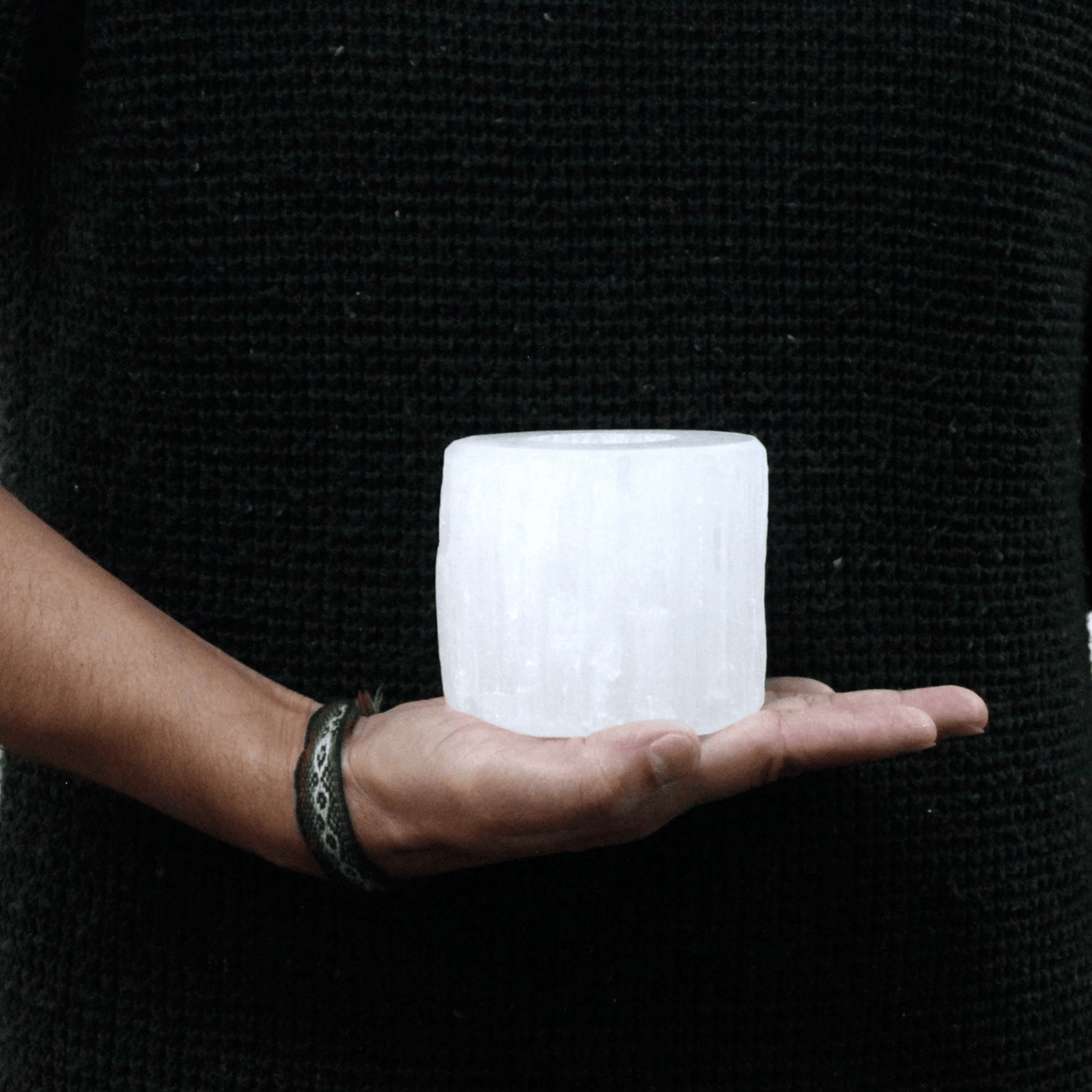 Person holding a textured white selenite cylinder shaped candle holder in front of a black background
