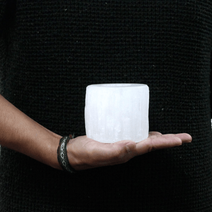 Person holding a textured white selenite cylinder shaped candle holder in front of a black background