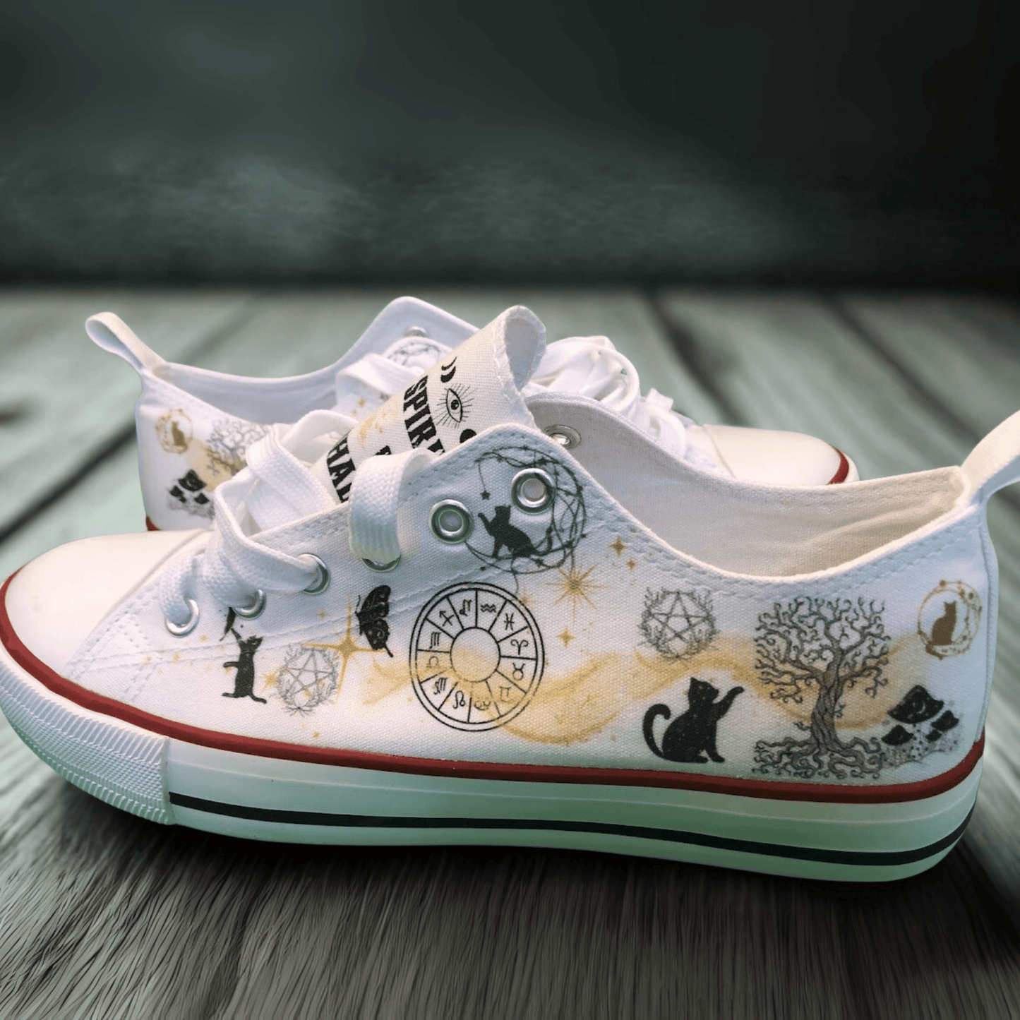 White canvas sneakers with black and gold witchy  illustrations on a wooden surface