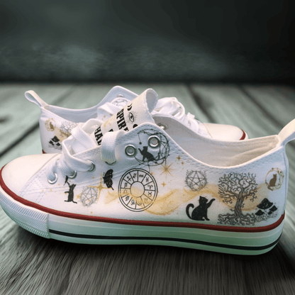 White canvas sneakers with black and gold witchy  illustrations on a wooden surface