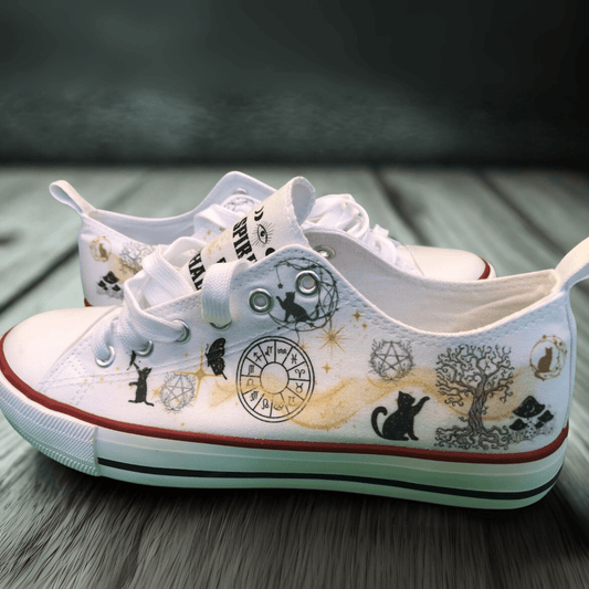 White canvas sneakers with black and gold witchy  illustrations on a wooden surface