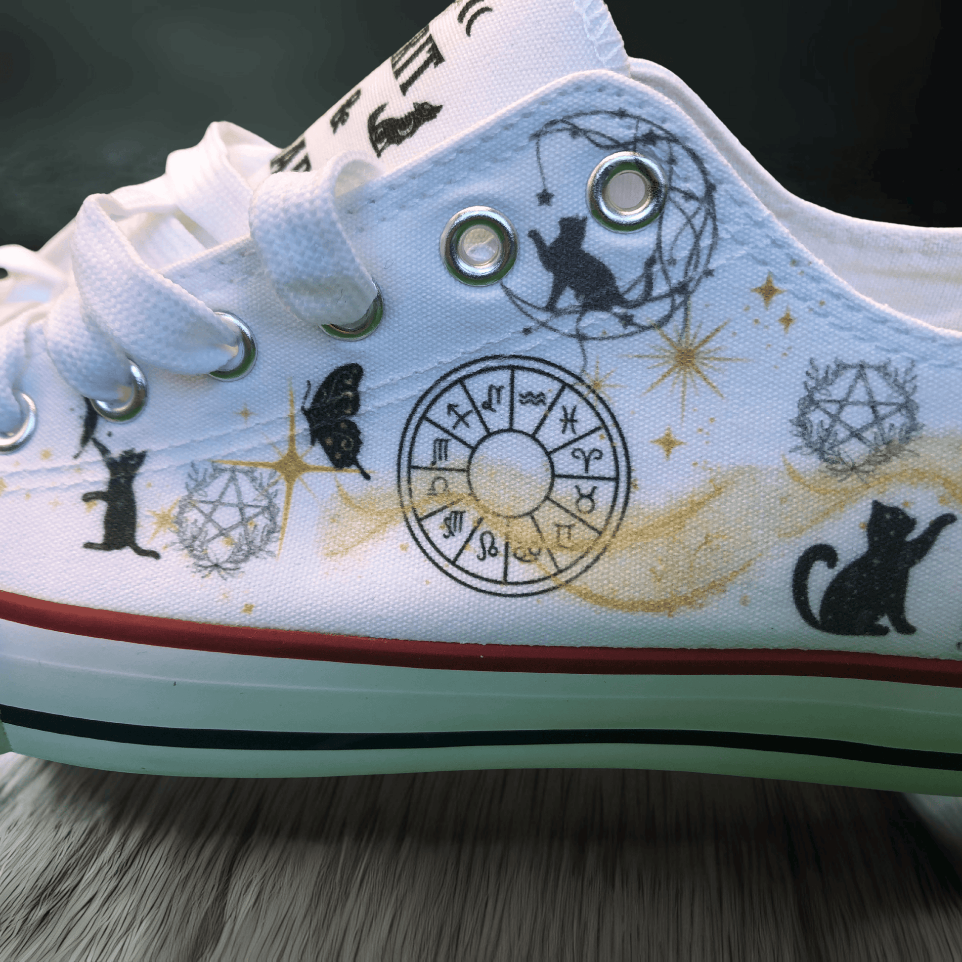 White sneaker with black cat and astrological symbol designs on a dark background