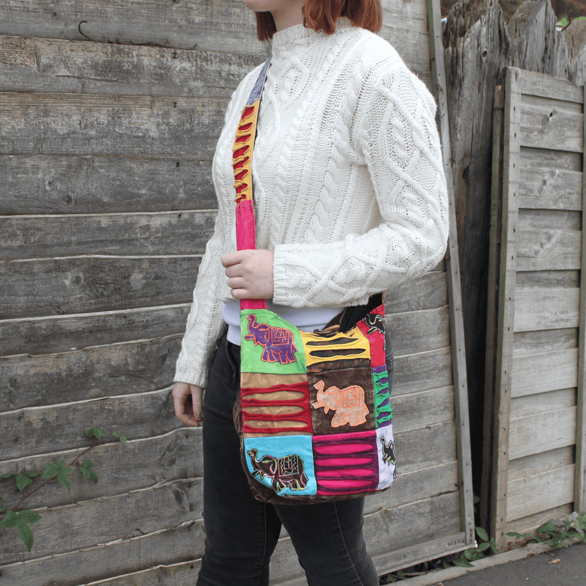 Person holding a colorful patchwork bag against a wooden fence.