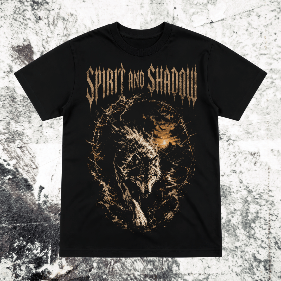 A black short-sleeve graphic t-shirt featuring the band name 'Spirit and Shadow' in a metallic gold font above a detailed graphic of a wolf surrounded by a fiery orange and gold circular design, displayed flat against a textured gray background.