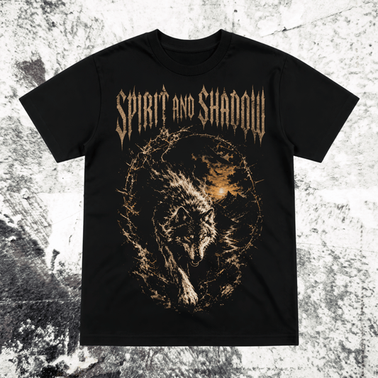 A black short-sleeve graphic t-shirt featuring the band name 'Spirit and Shadow' in a metallic gold font above a detailed graphic of a wolf surrounded by a fiery orange and gold circular design, displayed flat against a textured gray background.