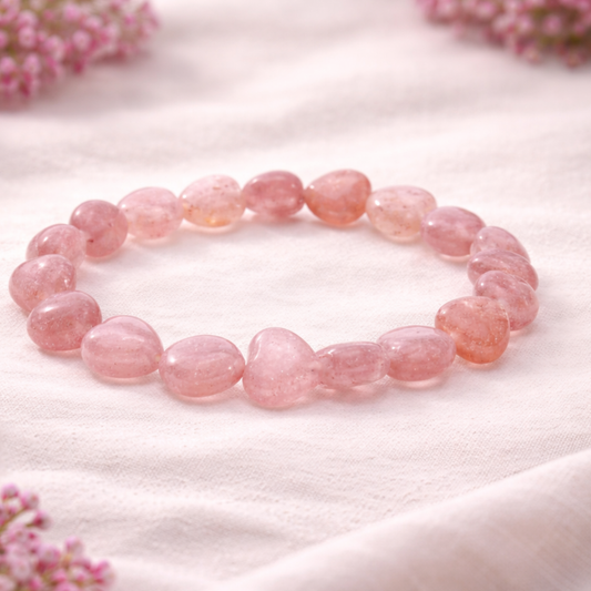 Pink strawberry quartz heart shaped beads bracelet on a white fabric background with pink flowers.