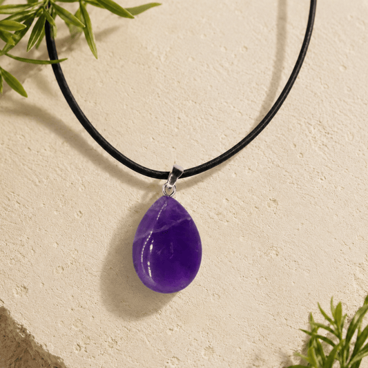 Purple teardrop pendant on a black cord against a beige background with green leaves.