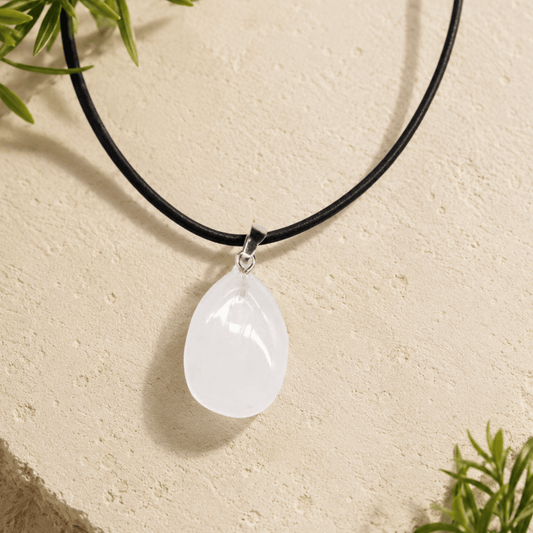Teardrop-shaped pendant on a black cord against a beige background with greenery.