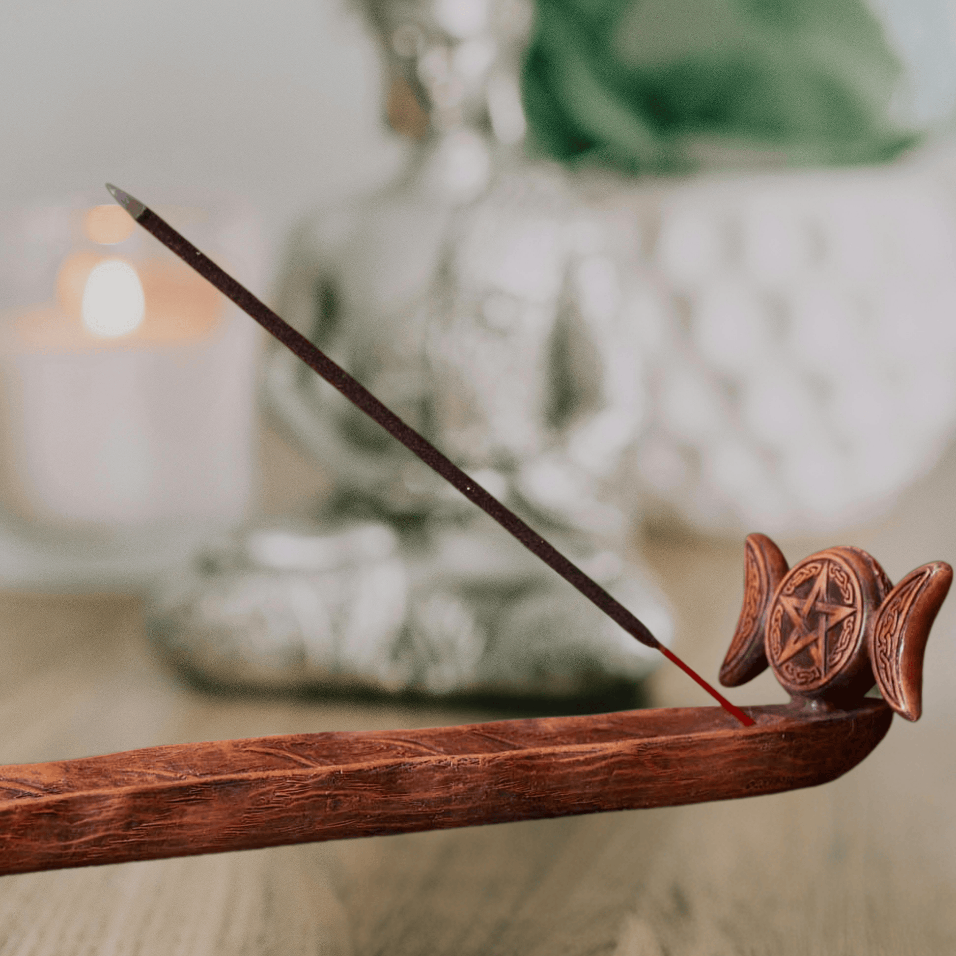 Wooden incense burner with a single incense stick, featuring a pentagram design, on a blurred background.
