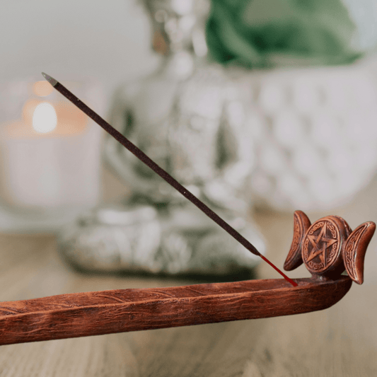 Wooden incense burner with a single incense stick, featuring a pentagram design, on a blurred background.