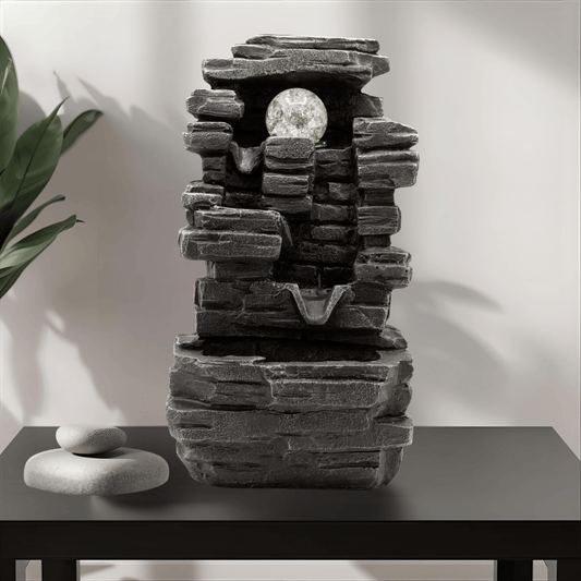 Decorative stone fountain on a table with a plant in the background