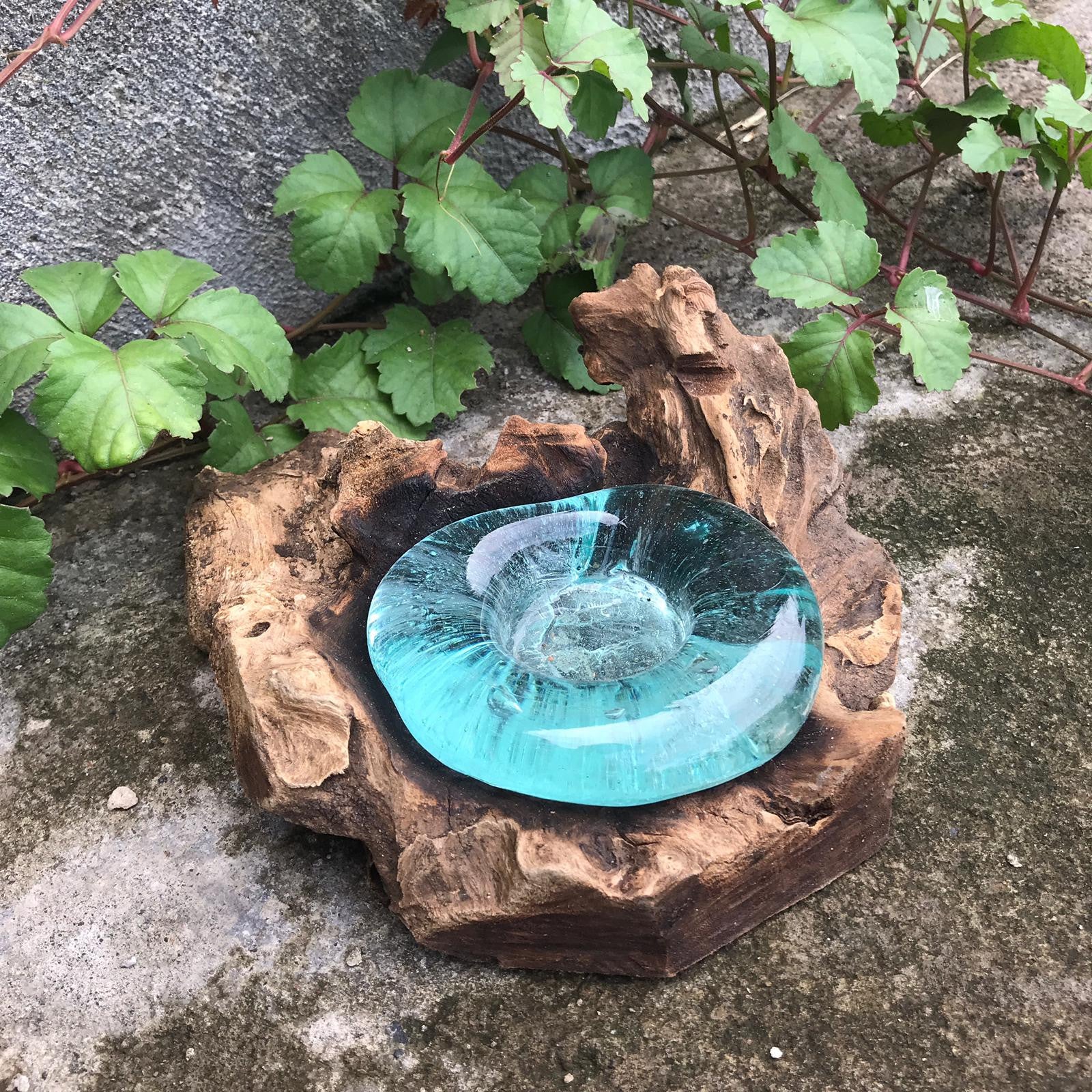 Turquoise glass bowl on a wooden log with greenery in the background