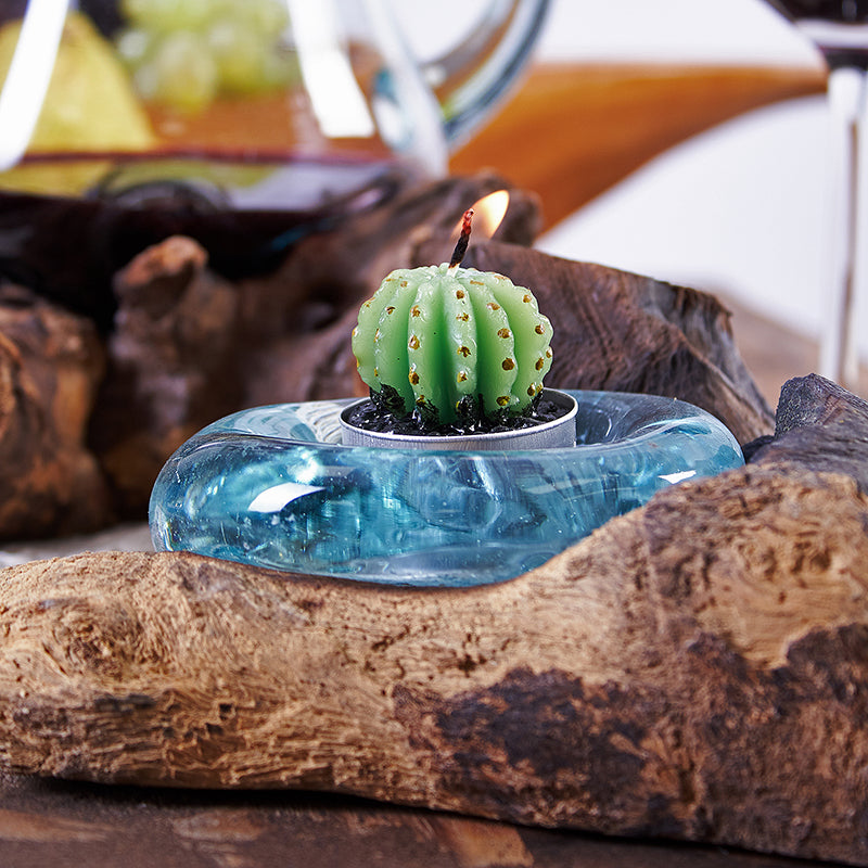 Candle shaped like a cactus in a blue holder on a wooden surface