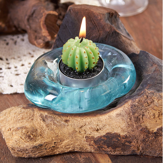 Candle in the shape of a cactus inside a blue glass holder on a wooden surface.